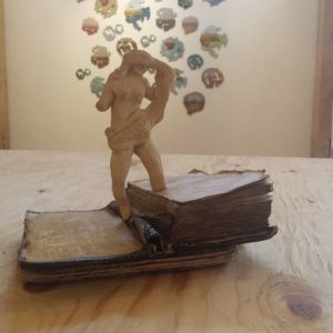 small stoneware figure that is blindfolded standing on an old book by Bunyan