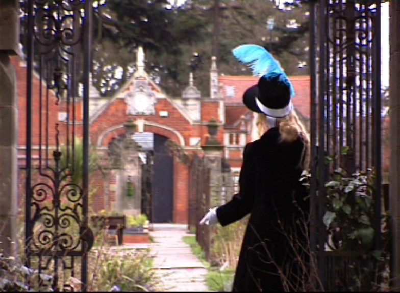 a picture of the artist dressed in Empire clothing in front of the gates to an old house