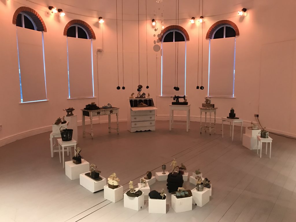small sculptures on white domestic furniture plinth in a circular gallery with light and sound