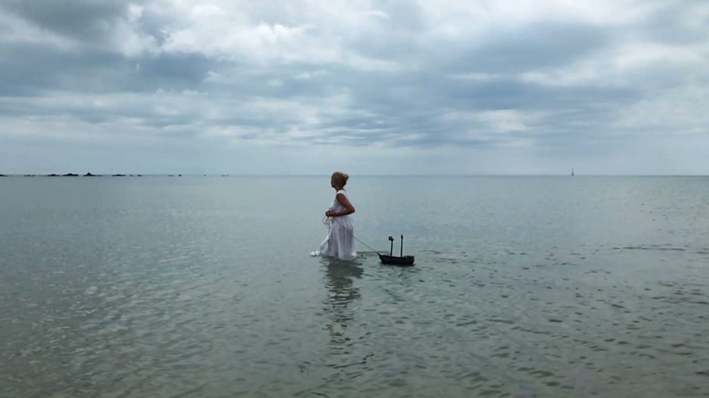 a woman pulling a toy boat in the sea with a moody sky in the background